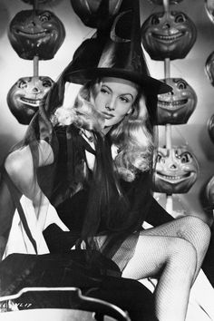 a black and white photo of a woman in a witch costume surrounded by pumpkins