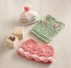 crocheted baby clothes and accessories are laid out on the floor next to a rubber stamp