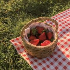 a basket full of strawberries sitting on top of a checkered table cloth in the grass