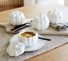 three white pumpkins sitting on top of a table next to a bowl of soup