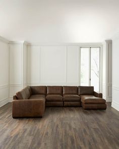 a large brown leather sectional sofa sitting on top of a hard wood floor in an empty room