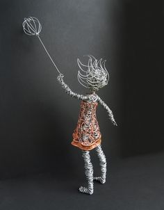 a wire doll holding a string ball in its hand and wearing a dress with an orange top