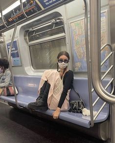 a woman sitting on a subway train with her face covered by a mask and black boots