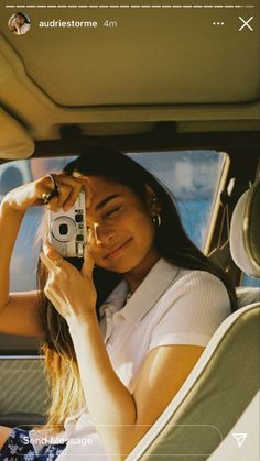 a woman sitting in the back seat of a car holding a camera up to her face