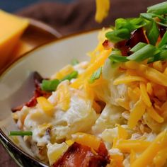 a white bowl filled with food on top of a wooden table next to cheese and green onions