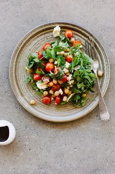 a salad with tomatoes, chickpeas and lettuce on a plate next to a cup of coffee