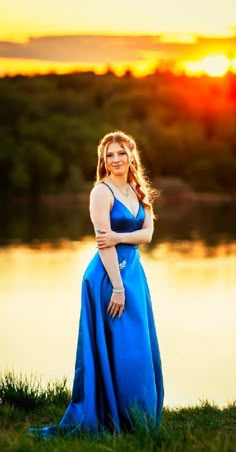 a woman in a blue dress is posing for a photo by the water at sunset