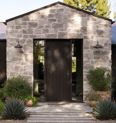 a stone house with two doors and steps leading up to the front door is surrounded by greenery