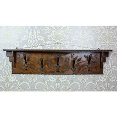 a wooden wall hanging with hooks and birds on it's side, in front of a damask wallpaper