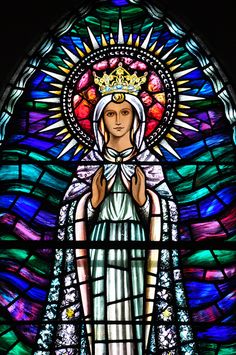 a stained glass window with an image of the virgin mary in white dress and crown on her head