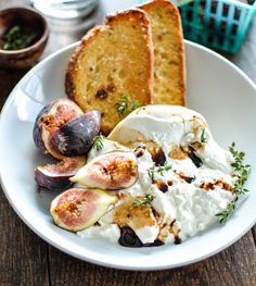 a white plate topped with bread and figs next to other food on top of a wooden table