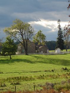 an old farm house sits in the middle of a green field with trees and grass