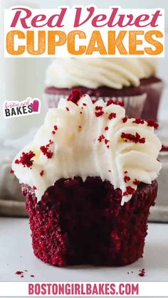 A close-up of red velvet cupcakes with luscious cream cheese frosting, one in the foreground with a bite taken out of it. In the background, more cupcakes sit on a metal tray. A bottle of milk and two glasses are visible on a white countertop and a tiled backsplash.