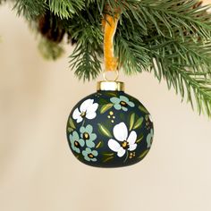 an ornament hanging from a christmas tree with green leaves and flowers on it