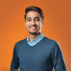 a man in a blue sweater smiles at the camera while standing against an orange background