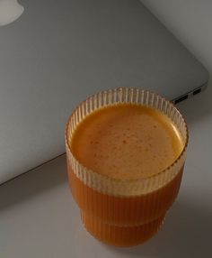 an orange cup sitting on top of a table next to a white laptop computer screen