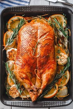 a roasted chicken in a roasting pan with lemons, onions and rosemary