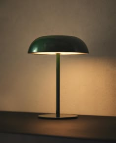 a green table lamp sitting on top of a wooden desk next to a white wall