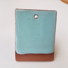 a blue and brown square shaped object sitting on top of a white surface with a small hole in the center