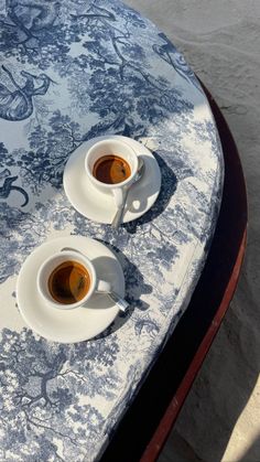 two cups of coffee sitting on top of a blue and white cloth covered tablecloth