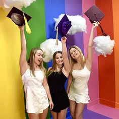 three girls in white dresses holding up graduation hats