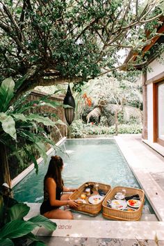 a woman sitting on the edge of a swimming pool with food in her basket next to it