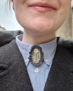 a close up of a person wearing a blue shirt and grey blazer with a button on it