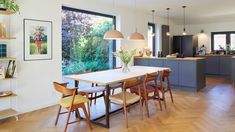 an open kitchen and dining room with wood flooring in the living area, along with large windows that look out onto trees