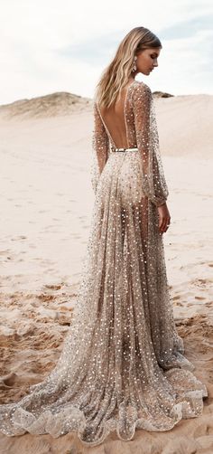 a woman standing on top of a sandy beach wearing a dress with long sleeves and sequins