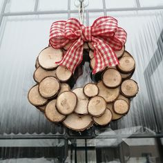 a wreath made out of logs with a red bow hanging from it's front door