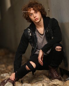 a young man sitting on top of a pile of rocks next to a cement wall