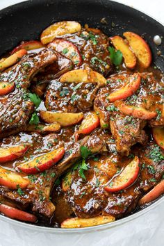 a skillet filled with meat and apples covered in gravy, garnished with parsley