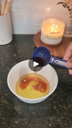 a person pours liquid into a bowl on a counter next to a lit candle