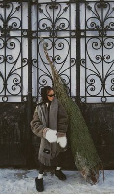 a woman is carrying a tree in front of an iron gate on a snowy day