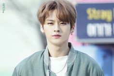 a young man in a green jacket is looking at the camera while wearing earrings