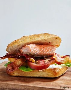 a sandwich with salmon, bacon and lettuce on it sitting on a cutting board