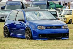 a blue car parked on top of a grass covered field next to other cars in the background