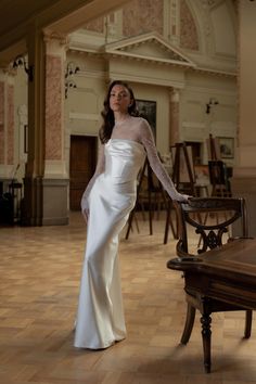 a woman in a long white dress standing next to a table with chairs on it