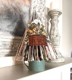 a christmas tree made out of magazines sitting on top of a white mantle next to a candle