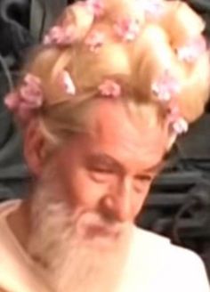 an old man with blonde hair and pink flowers in his hair is staring at the camera