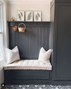 a bench with pillows on it in front of a window and some pictures above the bench