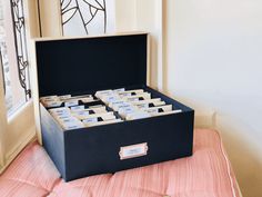 a black box filled with cards sitting on top of a pink bed sheet next to a window