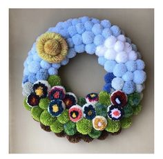 a wreath made out of yarn with flowers and leaves on the front, sitting on a wall