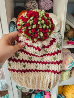 a hand is holding a knitted hat in front of yarns and crochet