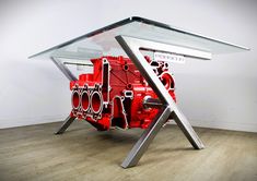 a red engine sitting on top of a wooden floor next to a glass table with metal legs