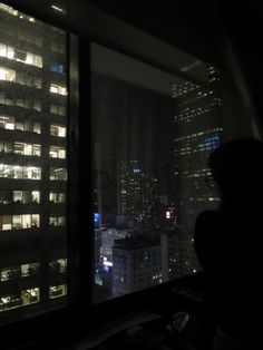 a person standing in front of a window looking out at the city lights and skyscrapers