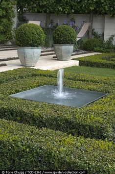 a fountain in the middle of a garden surrounded by hedges