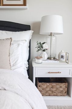 a bedroom with a white bed, nightstand and basket on the side table next to it