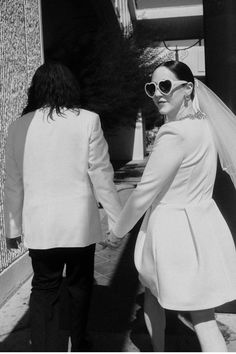 black and white photograph of two people in wedding attire walking down the street holding hands