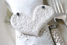 two white heart shaped cookies sitting on top of a plate next to a fork and knife